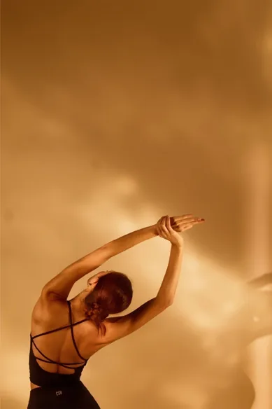 A student stretching one arm overhead in warm light